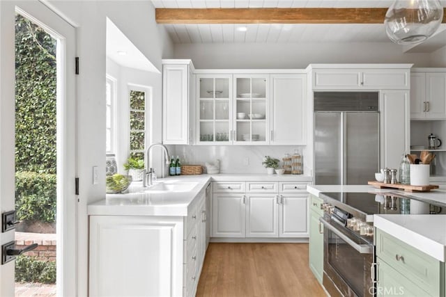 kitchen with a sink, stainless steel appliances, beam ceiling, and white cabinetry