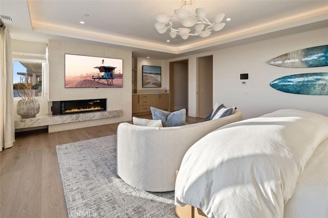bedroom with a chandelier, recessed lighting, a raised ceiling, a high end fireplace, and wood finished floors