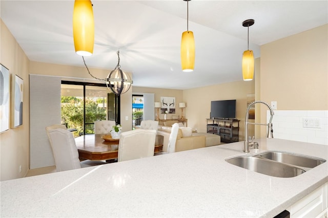 kitchen featuring a sink, an inviting chandelier, decorative light fixtures, and light stone countertops