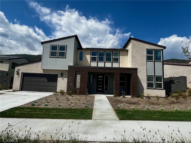 contemporary home featuring brick siding, a porch, driveway, and stucco siding