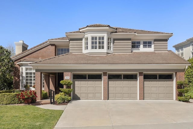 traditional-style house featuring brick siding, a tile roof, a garage, driveway, and a chimney