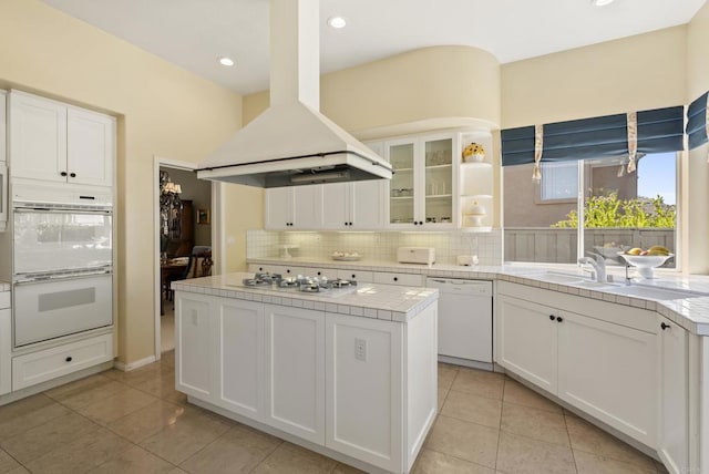 kitchen with white appliances, a kitchen island, white cabinets, decorative backsplash, and island range hood