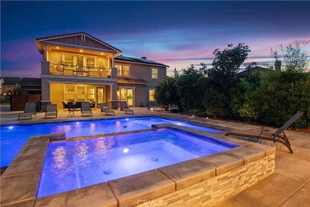 pool at dusk featuring a patio, an outdoor pool, and an in ground hot tub
