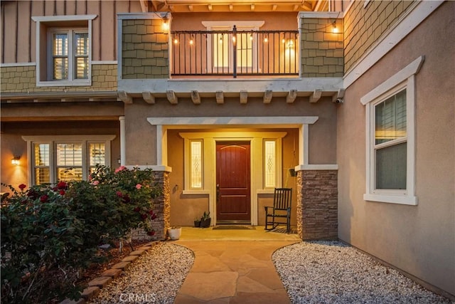 doorway to property with stone siding, stucco siding, and a balcony