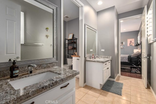 full bathroom featuring two vanities, ensuite bath, toilet, and a sink