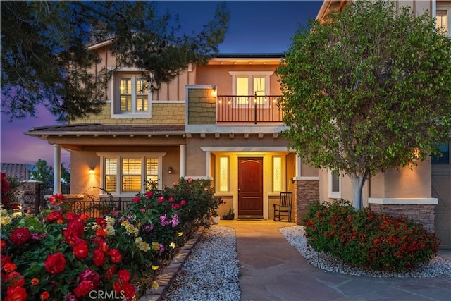 view of front of property featuring covered porch, stone siding, a balcony, and stucco siding