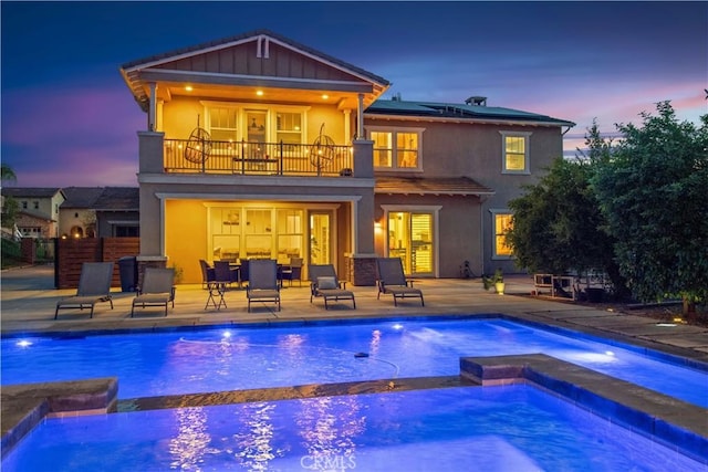 16550 Catalonia Dr, Riverside, CA 92504 - rear view of house featuring a balcony, roof mounted solar panels, a pool with connected hot tub, stucco siding, and a patio area