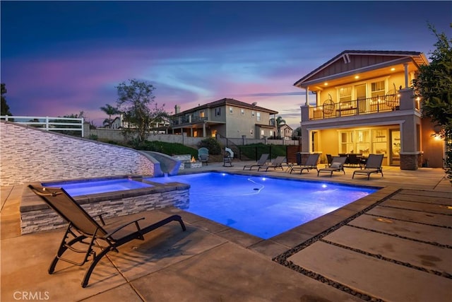 pool at dusk featuring a patio area, a water slide, a pool with connected hot tub, and a fenced backyard
