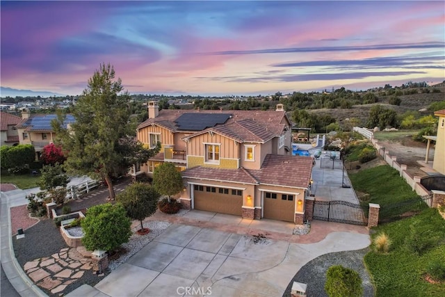 view of front of house with a gate, a chimney, roof mounted solar panels, concrete driveway, and fence
