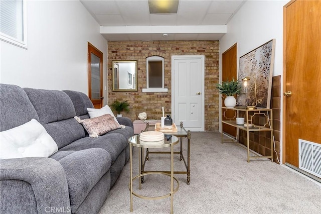carpeted living room featuring visible vents and brick wall
