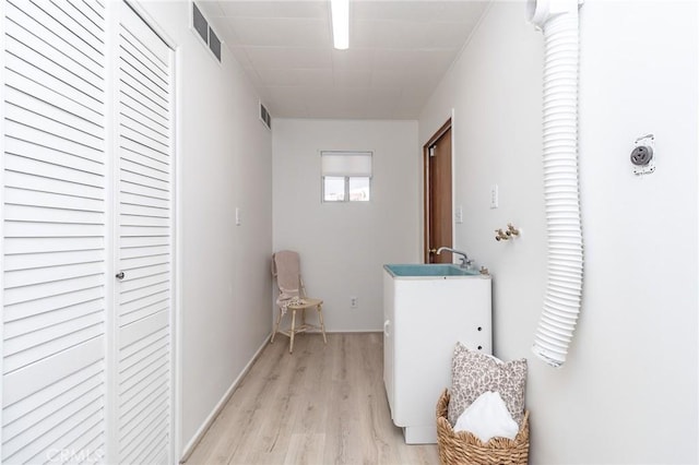 hall featuring light wood-style floors, a sink, and visible vents
