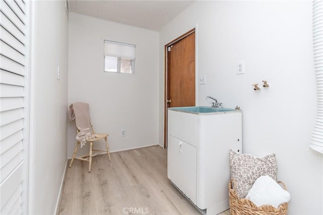 laundry area featuring light wood finished floors, a sink, and cabinet space