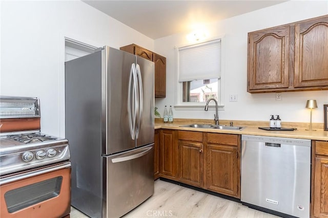 kitchen with brown cabinetry, appliances with stainless steel finishes, a sink, and light countertops