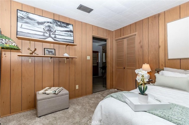 carpeted bedroom with a closet, wooden walls, and visible vents