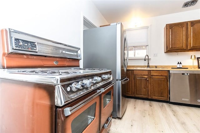 kitchen featuring light countertops, visible vents, appliances with stainless steel finishes, light wood finished floors, and a sink