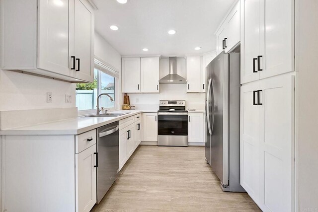 kitchen featuring white cabinets, stainless steel appliances, wall chimney range hood, a sink, and light wood-style flooring