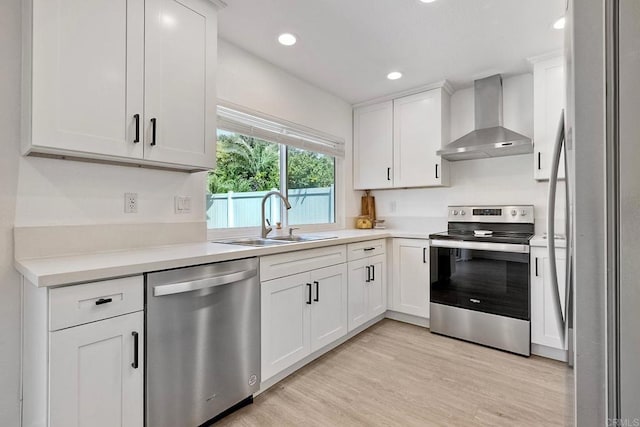 kitchen with wall chimney range hood, a sink, stainless steel appliances, light countertops, and white cabinetry