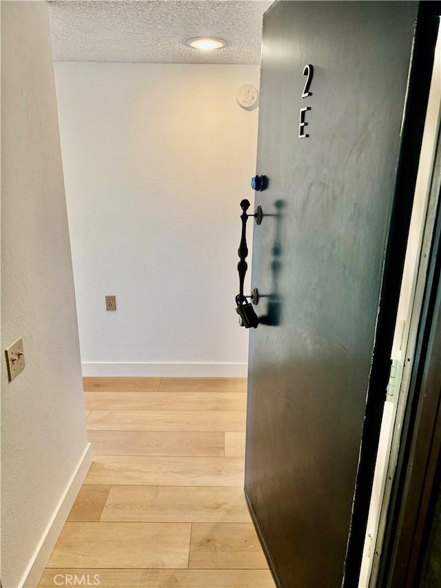 hallway with light wood finished floors, a textured ceiling, and baseboards