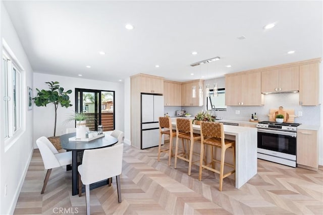 kitchen featuring stainless steel gas stove, freestanding refrigerator, light brown cabinetry, recessed lighting, and light countertops
