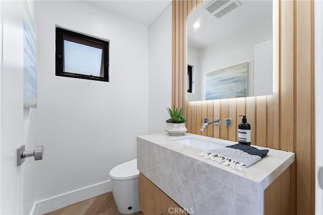 half bath featuring visible vents, baseboards, toilet, vanity, and wood finished floors
