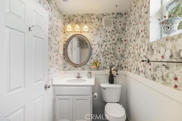 bathroom with vanity, visible vents, toilet, and wallpapered walls