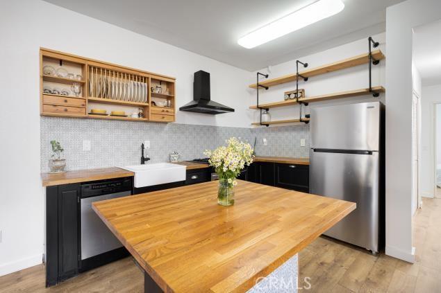 kitchen featuring open shelves, wall chimney range hood, dark cabinetry, a sink, and stainless steel appliances