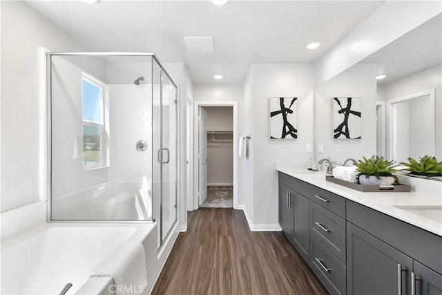 full bathroom featuring double vanity, a shower stall, a bath, a sink, and wood finished floors