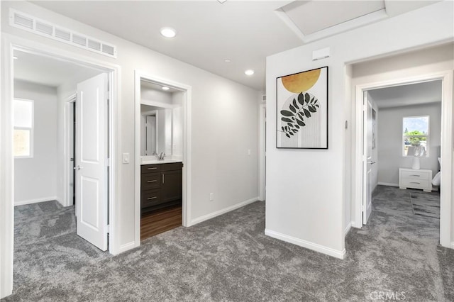 hall with visible vents, carpet floors, attic access, a sink, and baseboards