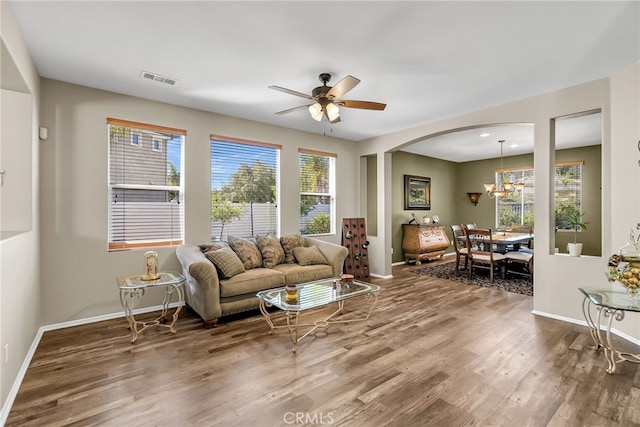 living room with ceiling fan with notable chandelier, arched walkways, visible vents, wood finished floors, and baseboards