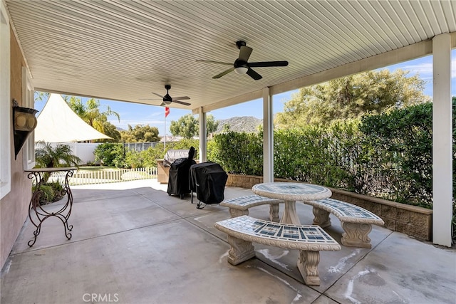 view of patio with ceiling fan, a grill, a fenced backyard, outdoor dining space, and a mountain view