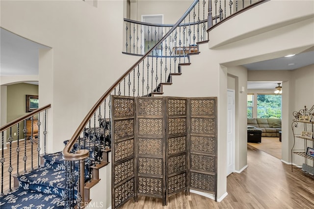 stairs with arched walkways, a towering ceiling, a ceiling fan, and wood finished floors
