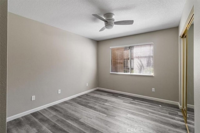 unfurnished bedroom featuring baseboards, a closet, a textured ceiling, and wood finished floors