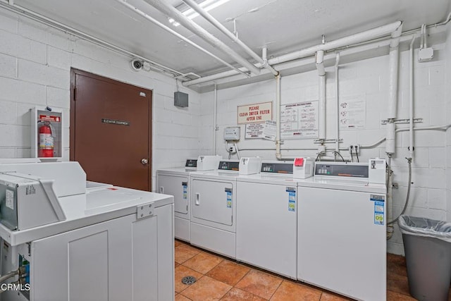 shared laundry area with light tile patterned floors, concrete block wall, and independent washer and dryer