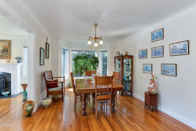 dining room featuring light wood-style floors, a high end fireplace, an inviting chandelier, and baseboards