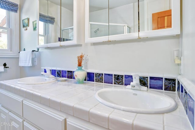 full bath featuring double vanity, a tile shower, and a sink