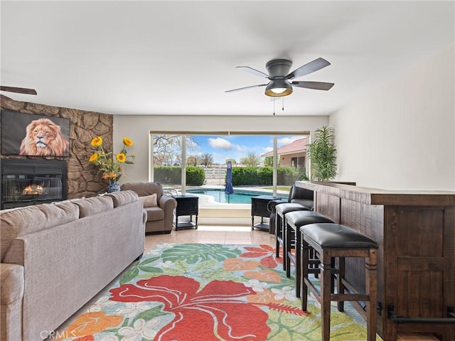 living area with a bar, a ceiling fan, and a stone fireplace