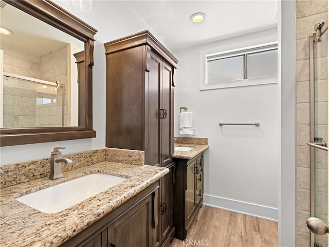 bathroom with two vanities, baseboards, a stall shower, a sink, and wood finished floors