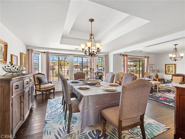 dining space with a tray ceiling, a notable chandelier, and dark wood-style floors