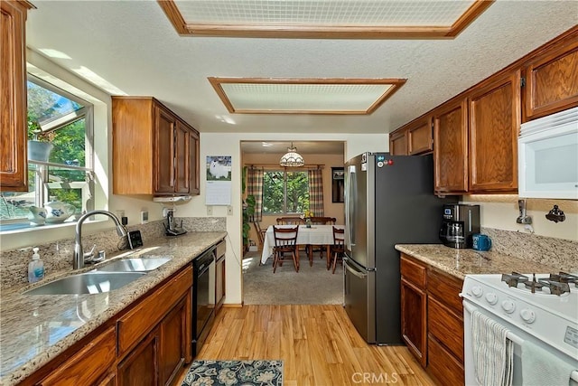 kitchen with a sink, light wood-type flooring, white appliances, brown cabinets, and light stone countertops