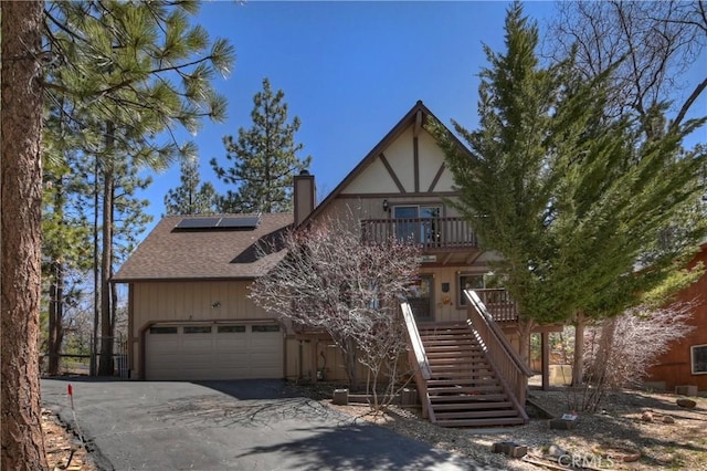 view of front of house featuring roof with shingles, a chimney, an attached garage, aphalt driveway, and solar panels