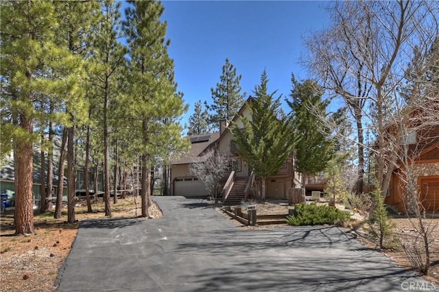 view of property hidden behind natural elements with driveway and roof mounted solar panels