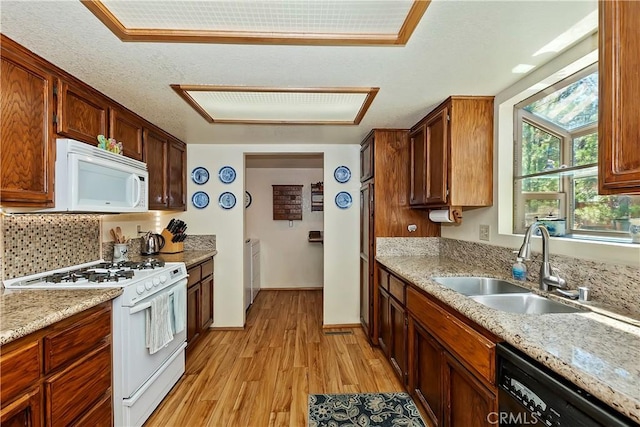 kitchen featuring white appliances, light stone counters, a sink, light wood finished floors, and decorative backsplash