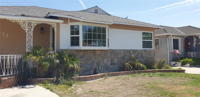 view of side of property featuring a shingled roof and stone siding
