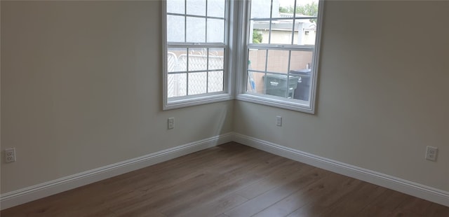 spare room with baseboards, wood finished floors, and a healthy amount of sunlight