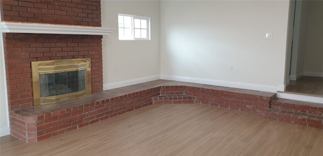 unfurnished living room featuring a brick fireplace, wood finished floors, and baseboards