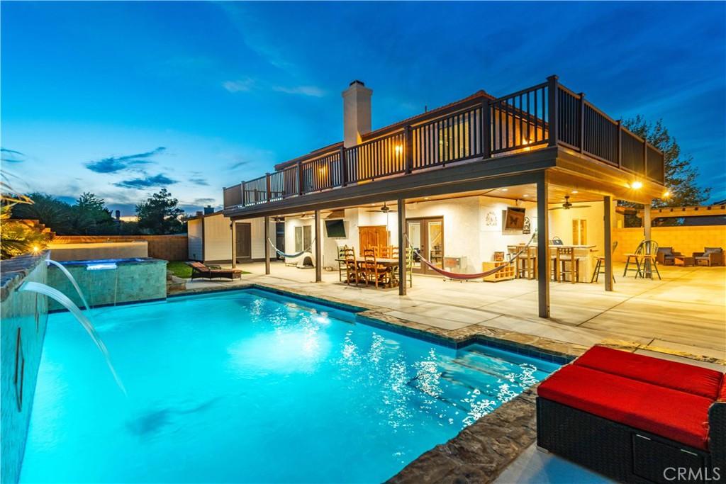 back of property with a ceiling fan, a patio, outdoor dining area, a balcony, and a fenced in pool