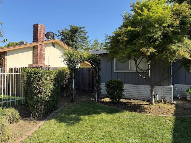 exterior space with board and batten siding, a chimney, brick siding, fence, and a yard