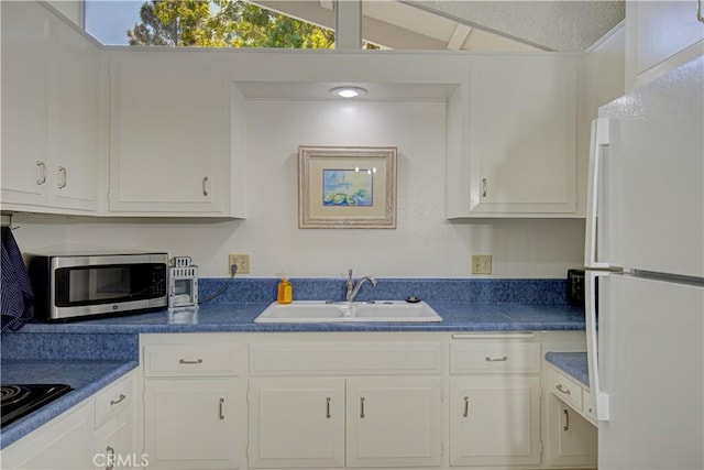 kitchen with stainless steel microwave, white cabinets, a sink, and freestanding refrigerator