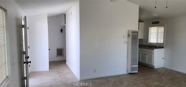 interior space featuring visible vents, baseboards, a sink, vaulted ceiling, and a heating unit