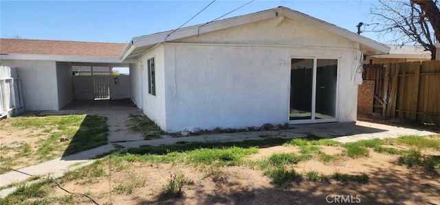 rear view of house featuring stucco siding and fence